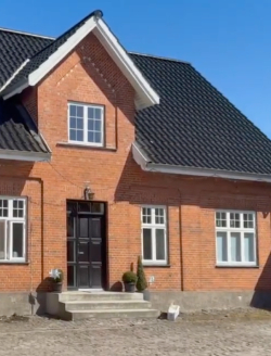 Rødt murstenshus med sort tag og hvide vinduer. kanap på 1. sal