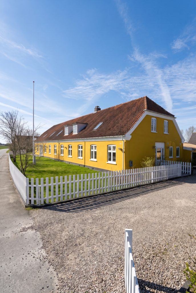 Samala Børneungehjem Bakkerupvej Stort gultpudset hus med rødt tag og to kanapper og hvide vinduesrammer. Der er flagstang i haven og hvidt statik omkring