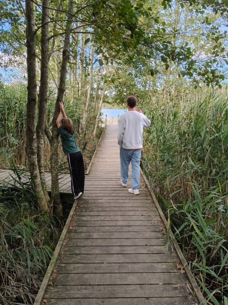 Samala_ Børne-Ungehjem Bakkerupvej4 Gangbro af træ ned mod skovsø, dreng læner sig op af træ og mand går med ryggen til