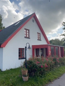 Gavl på hvidt hus med røde sternbrædder og sort tag. vinduer er rødmalede